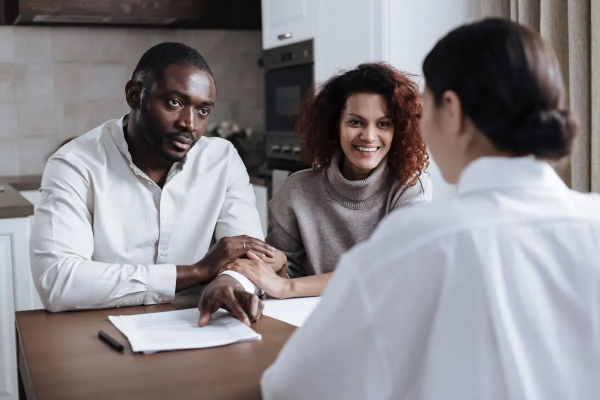 Couple reviewing financial documents with their advisor at a kitchen table